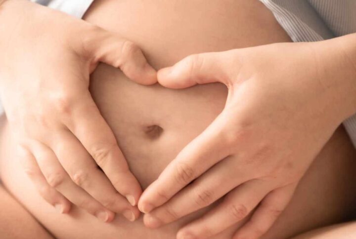 mains qui forment un cœur sur le ventre d'une femme enceinte. ventre de femme enceinte. chemise ouverte sur le ventre