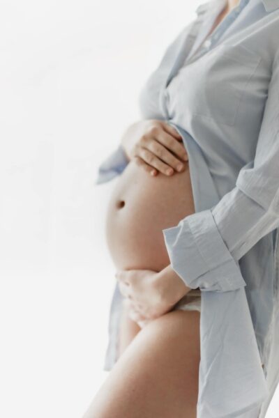 photo d'une femme enceinte, on ne voit pas son visage. Elle porte une chemise bleue, ouverte à partir de sous sa poitrine. elle a une main au dessus de son ventre et une main en dessous.