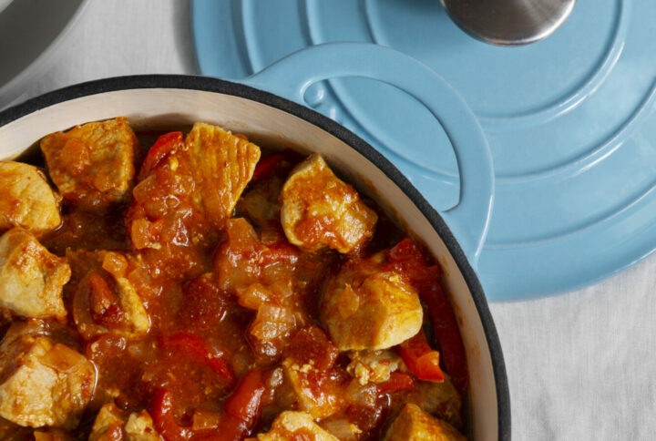 cocotte bleu dans lequel on voit un petit plat. De la viande blanche, de la tomate, de la sauce.