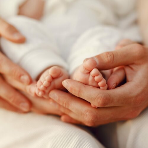 mains adultes avec au creux des petits pieds de bébé. Gros plan sur les mains, on ne voit pas le reste du corps.
