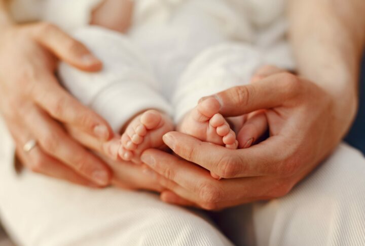 mains adultes avec au creux des petits pieds de bébé. Gros plan sur les mains, on ne voit pas le reste du corps.