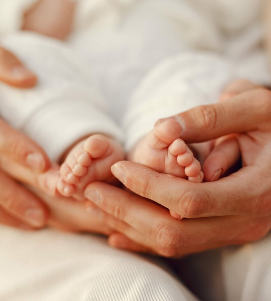 mains adultes avec au creux des petits pieds de bébé. Gros plan sur les mains, on ne voit pas le reste du corps.