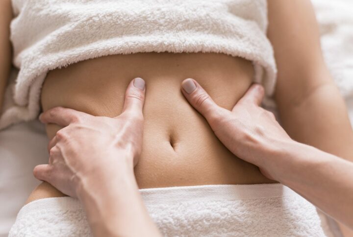 gros plan sur des mains qui massent un ventre. Il y a une serviette sur la poitrine et sur le pubis.