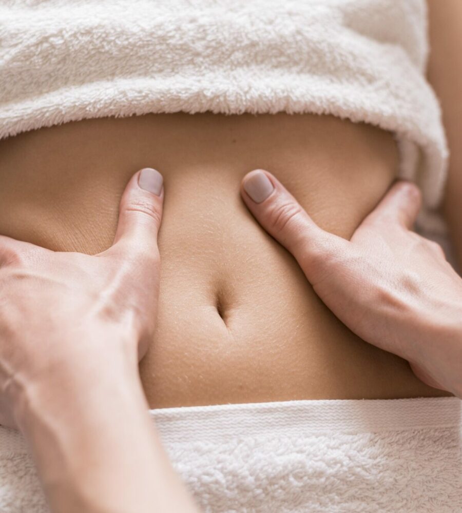 gros plan sur des mains qui massent un ventre. Il y a une serviette sur la poitrine et sur le pubis.